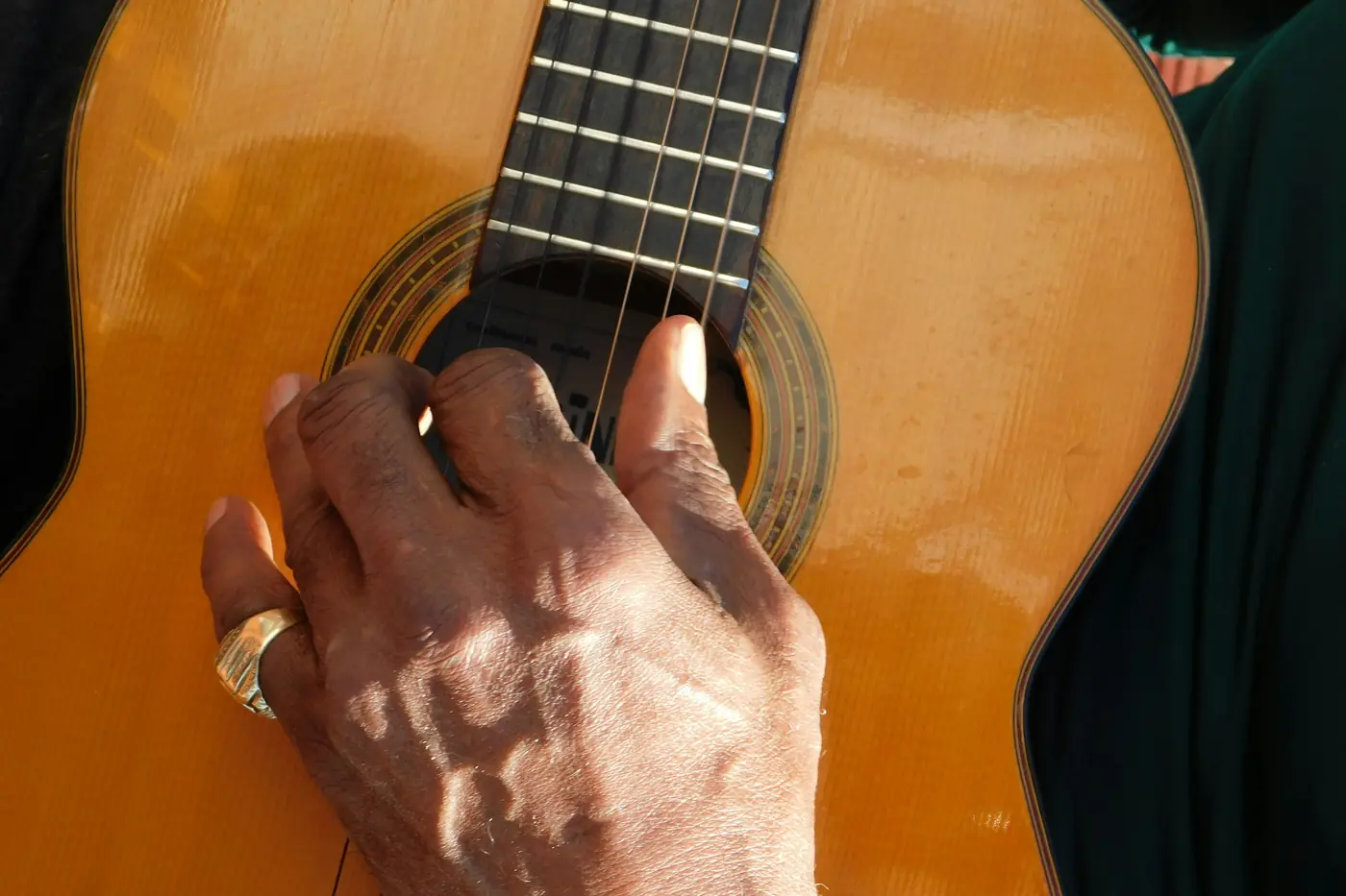 Detail ruky stiskající struny oranžovohnědé flamenkové kytary nad ozvučným otvorem.